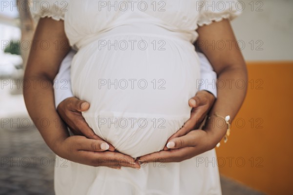 Pregnant woman with her partner holding her belly in the nature