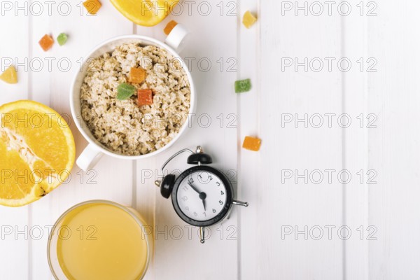 Orange glasses oatmeal porridge with alarm clock white table