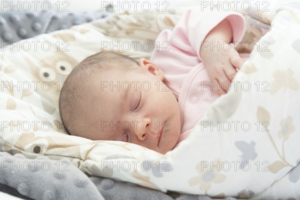 Sleeping newborn baby. Cute little girl one week old at home. Adorable lying on side covered with blanket. No retouch, newborn dry skin
