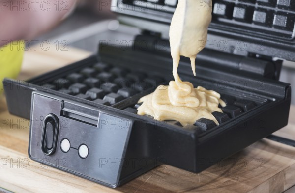 close-up of pouring dough into waffle iron, preparing homemade Belgian waffles