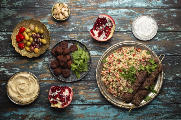 Various Turkish dishes: meat kebab with tabbouleh salad, falafel, hummus, olives, pistachios and other Middle Eastern meze on wooden table top view. Ethnic arab food, cuisine of Turkey