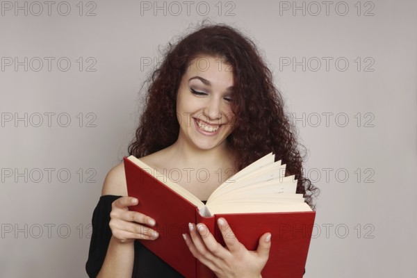 smiling teenage girl enjoys reading a funny hardcover book