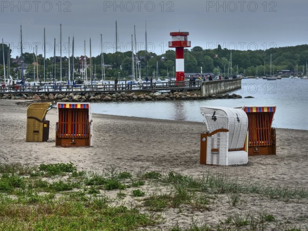Beach with beach chairs, in the background a lighthouse and boats, overcast sky, eckernförde, schleswig-holstein, germany