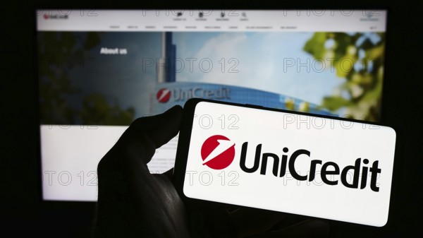 Stuttgart, Germany, 06-17-2023: Person holding mobile phone with logo of Italian financial company UniCredit S.p.A. on screen in front of web page. Focus on phone display, Europe