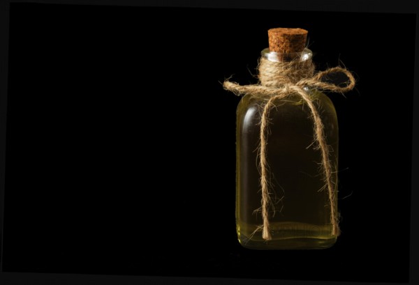 Close-up of a glass bottle with olive oil and cork stopper isolated on a black background
