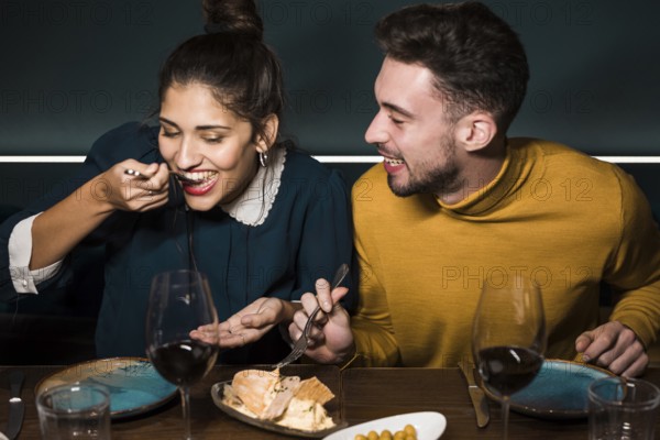 Young smiling man looking woman with forks tasting cheese table restaurant