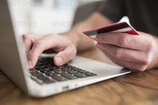 online shopping concept, person entering payment information on laptop computer holding debit or credit card in other hand