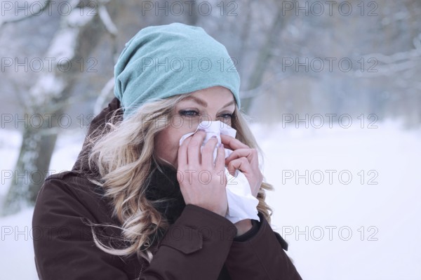 woman blowing her nose into paper tissue in winter