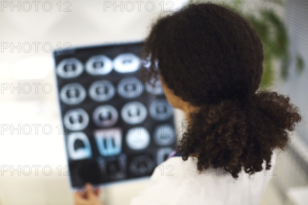 Rearview of ethnic female doctor analyzing X-ray or MRI scan while working in hospital, selective focus. Physician looking at CT screening, using diagnostic tool for detecting lung diseases