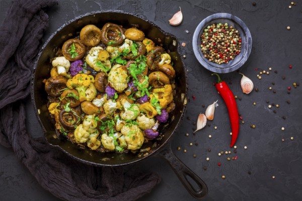 Roasted mushrooms and cauliflower, with onion, garlic and herbs in pan on black background
