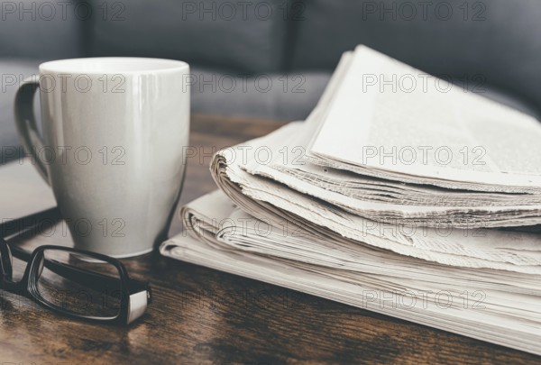 close-up shot of stack of newspapers, coffee mug and glasses on living room table