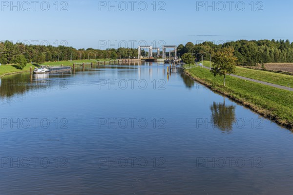 A water channel with a lock and bridge, surrounded by nature under an expansive sky