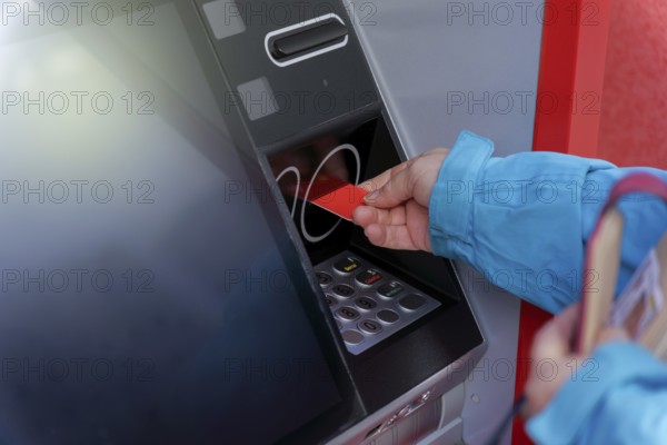 Woman in blue jacket inserting her credit card into an ATM to withdraw cash