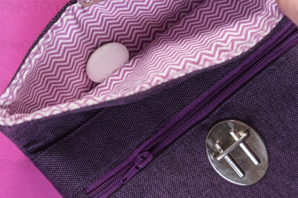 An Apple Air Tag lies in a purple clutch against a plain pink background