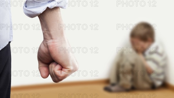 Family violence and aggression concept, furious angry man raised punishment fist over scared or terrified child boy sitting at wall corner