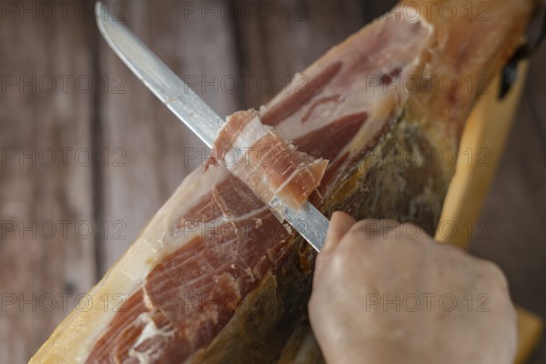 Spanish acorn-fed iberian ham close-up open knife cut by the hands of a charcuterie woman