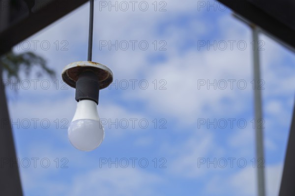 Light bulb hanging from a wire with a rusty lamp over a blue sky with clouds