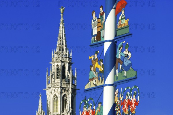 Maypole on Viktualienmarkt with musicians, dancing couple, market woman, waitress of Oktoberfest, tower of new town hall in background, Munich, Bavaria, Germany, Europe