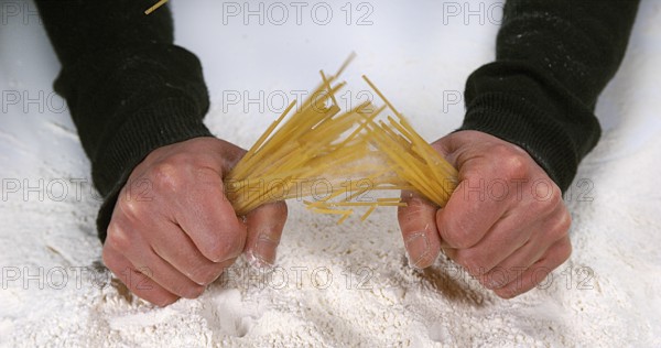 Hands of Man Breaking Spaghetti Pasta against Flour Background