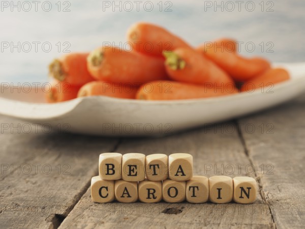 Wooden dices with the German words beta carotene and fresh carrots in the back, healthy eating concept