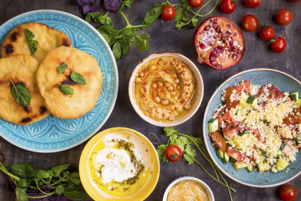 Table served with middle eastern traditional vegetarian dishes. Hummus, tahini, pitta, couscous salad and buttermilk dip with olive oil. Dinner party
