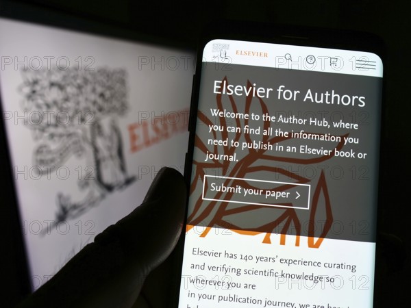 Stuttgart, Germany, 07-31-2022: Person holding smartphone with website of academic publishing company Elsevier on screen in front of logo. Focus on center of phone display, Europe