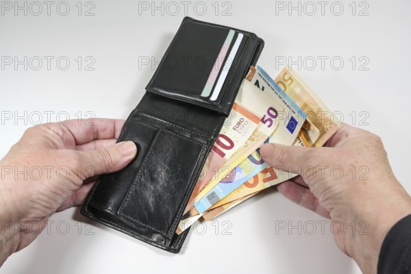 Hands taking various euro banknotes out of a black leather wallet, money and finance concept, light gray background, selected focus, narrow depth of field