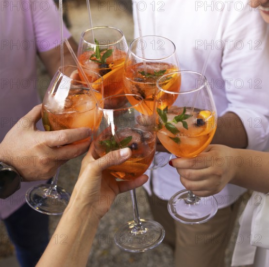 Happy friends spending time together, focus on young women drinking Aperol spritz cocktail. Summer wedding party. Happiness and celebration concept