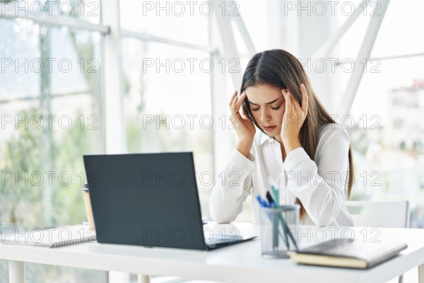 Stressed tired businesswoman sitting at her desk in modern office. Problems, pain concept