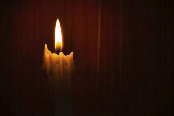 Single yellow wax candle burning alone in the dark red background. Conceptual image symbolize peace, love, hope or patience with free copy space