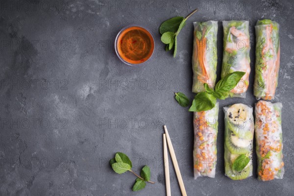 Fresh assorted spring rolls set background. Handmade asianChinese spring rolls, sauce, chopsticks. Rustic concrete background. Spring rolls with shrimps, vegetables, fruits. Space for text. Top view