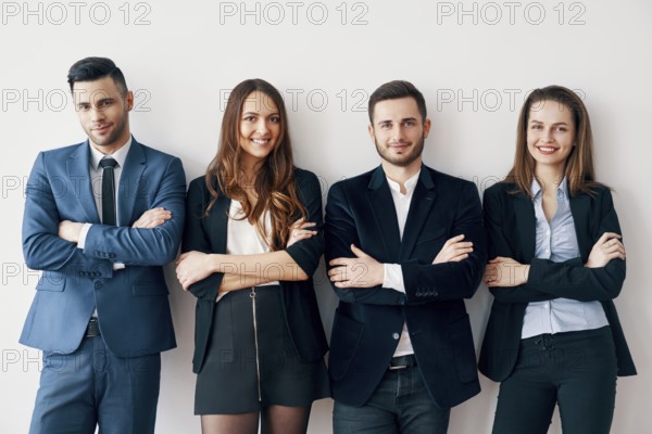 Young smiling business people with arms crossed lean to wall in office. Success teamwork concept