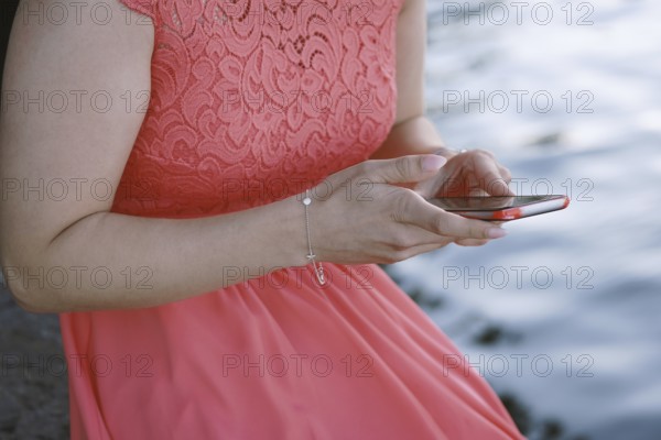 unrecognizable young woman sitting by the water using her smartphone or mobile phone
