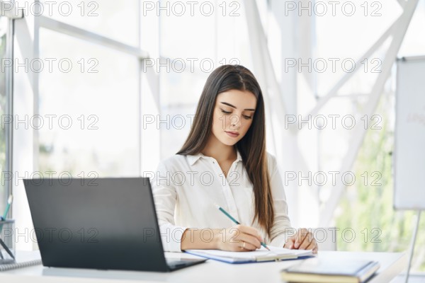 Pretty businesswoman with laptop and papers working at modern office. Woman signing contract and working on documents at her desk