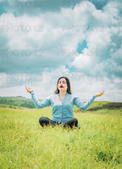 Portrait of relaxed young woman doing yoga in a field. Beautiful girl meditating on the grass in a beautiful field