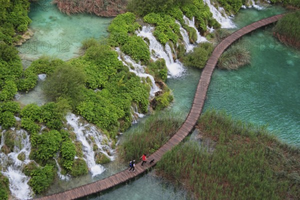 Wooden footbridge with hikers over turquoise ponds and waterfalls at Plitvice Lakes, Croatia, Europe