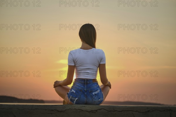 Rear view of a woman in meditation pose on the pier during summer sunset