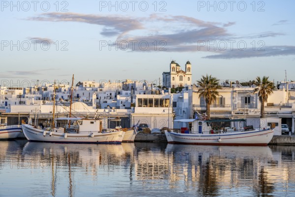 View of Naoussa, Fishing boats in the harbour at sunset, reflected in the sea, White Cycladic houses and church Agios Faneromeni, Naoussa, Paros, Cyclades, Greece, Europe