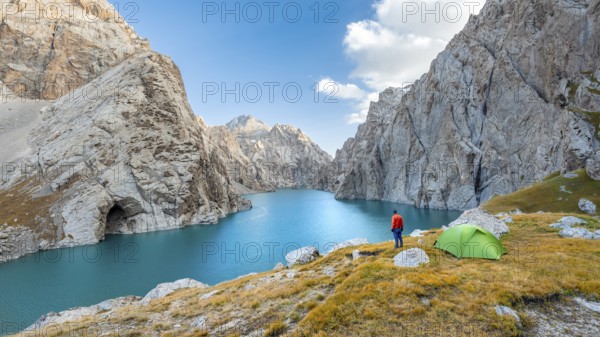 Young man with green tent at the turquoise mountain lake Kol Suu with rocky steep mountains, Kol Suu Lake, Sary Beles Mountains, Naryn Province, Kyrgyzstan, Asia