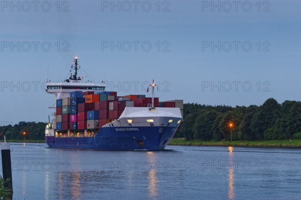 The container freighter Katharina Schepers sails towards the Elbe on the Kiel Canal in the late evening. Sehestedt, Schleswig-Holstein, Germany, Europe