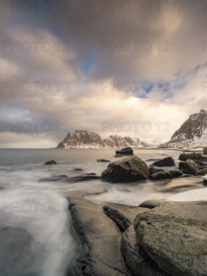 Rounded rocks on Utakleiv beach in a dramatic cloudy atmosphere, snow-capped mountains in the background, Vestvagoy Island, Lofoten, Norway, Europe