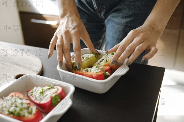 Close-up of female hands arranging stuffed bell peppers in ceramic baking tray