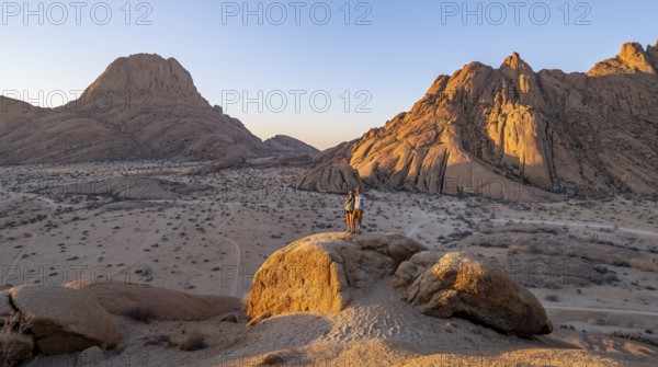 Couple on a mountain at sunset, summit of the Great Spitzkoppe and Pontoks in the background, eroded rocks, Spitzkoppe National Park, Erongo, Namibia, Africa