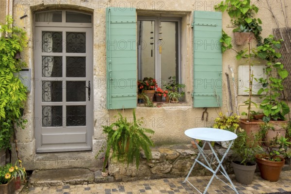 An old house façade with green shutters, numerous plants and a small round table, Vauvenargues, Provence-Alpes-Cote d'Azur, France, Europe