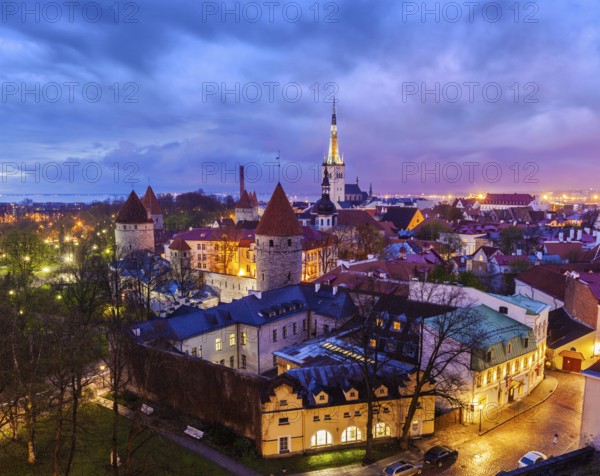 Aerial view of Tallinn Medieval Old Town with St. Olaf's Church and Tallinn City Wall illuminated in evening with dramatic cloudscape, Estonia, Europe