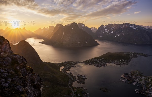 Mountain landscape, view from Reinebringen mountain to the village of Reine and Gravdalsbukta (Gravdals Bay), Olstinden mountain in the centre, Lilandstinden mountain on the right. On the left the Reinefjord with other mountains. At night at the time of the midnight sun in good weather. The sun is above the mountains. Early summer. Reine, Moskenesoya, Lofoten, Norway, Europe