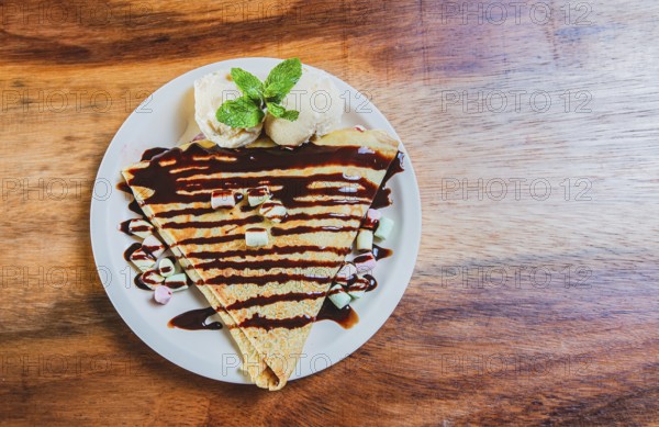 Top view of chocolate crepe with ice cream on wooden table. High angle view of chocolate crepe with ice cream on wooden background
