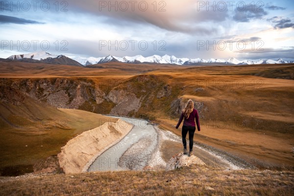 Glaciated and snow-capped mountains, Young woman in mountain landscape with yellow grass in the morning light, Tian Shan, Sky Mountains, Sary Jaz Valley, Kyrgyzstan, Asia