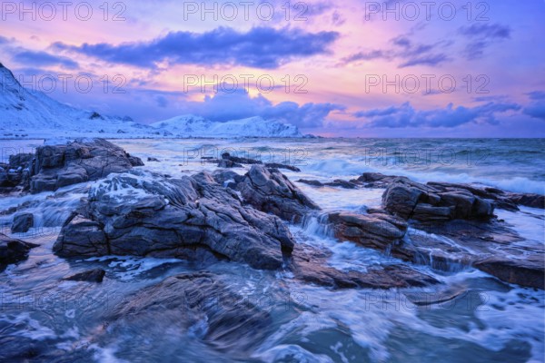 Waves of Norwegian sea on rocky coast in fjord on sunset with sun. Skagsanden beach, Lofoten islands, Norway, Europe