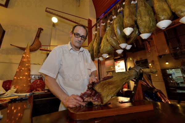 Waiter cuts ham in the "La Boveda" tapas bar, La Lonja district, Palma, Mallorca, Balearic Islands, Spain, Europe